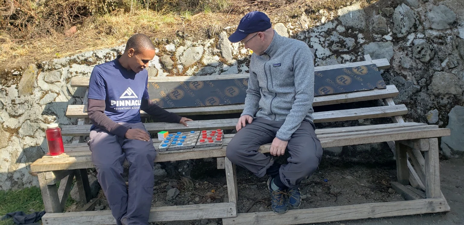 Two people playing draughts on a bench beside a stone wall